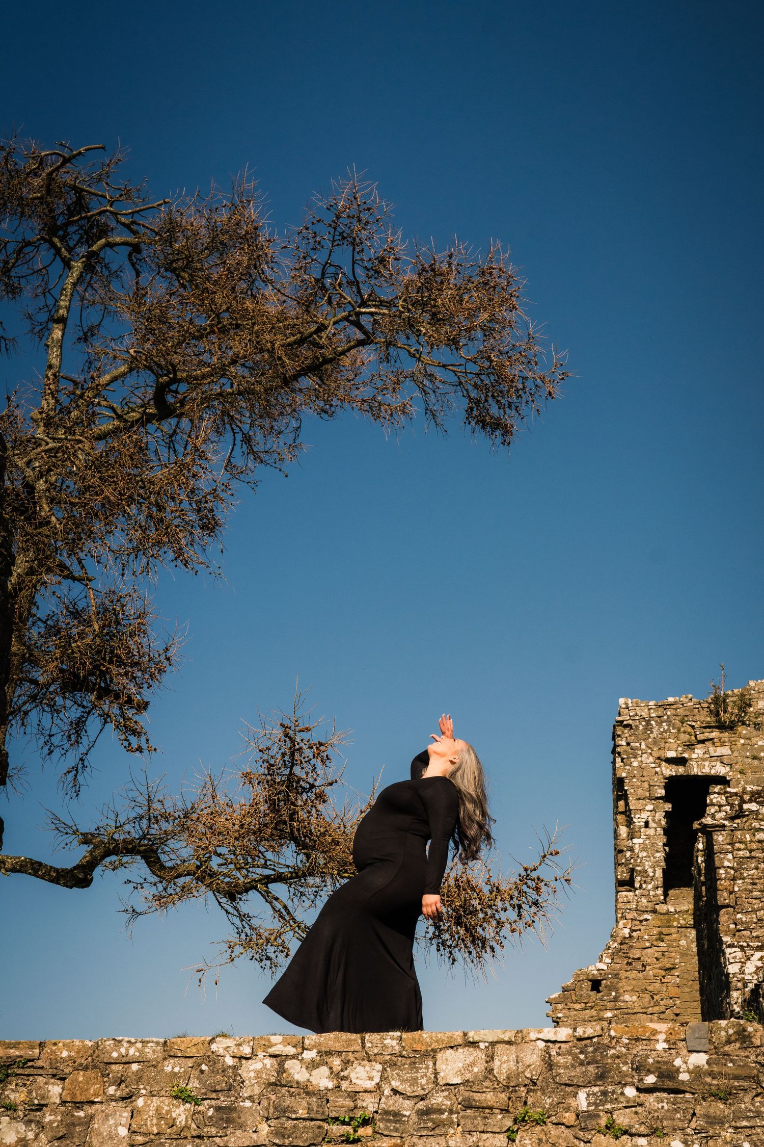 Figure silhouettes against blue sky on ancient stone castle walls with autumn tree branches. Family PHOTOGRAPHER Dublin