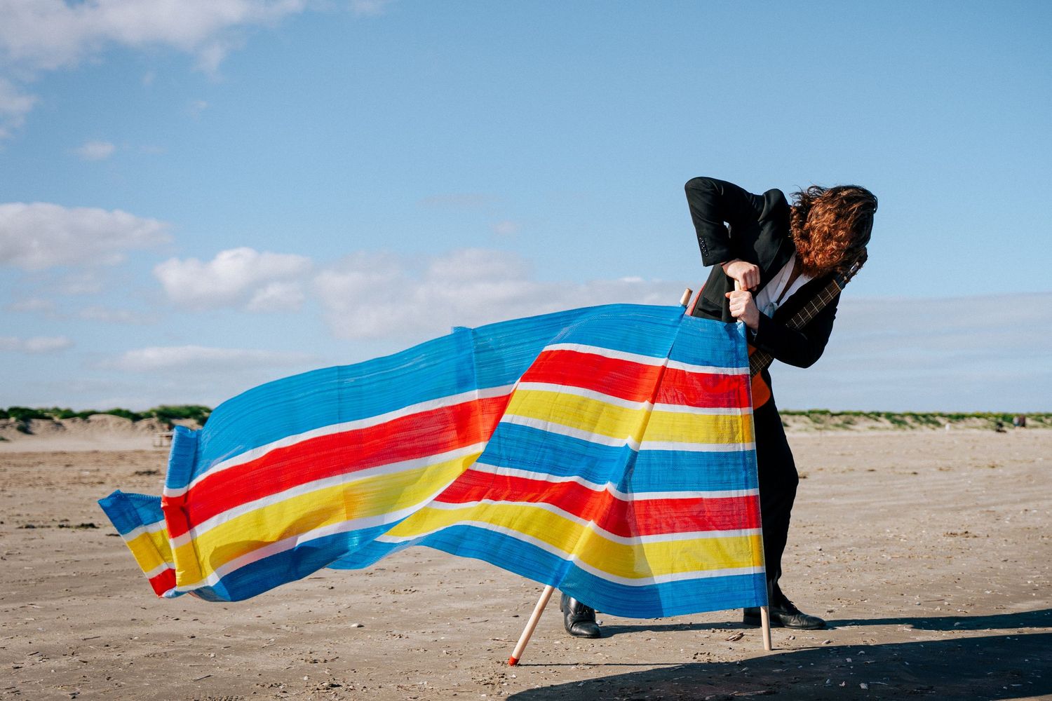 A colorful striped beach towel or blanket blows in the wind on a sandy beach. PHOTOGRAPHER Dublin