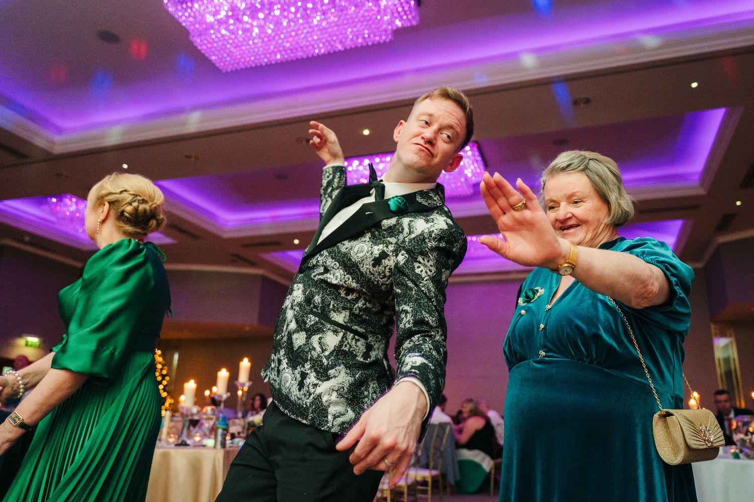 Wedding celebration panorama showing guests dancing under purple chandeliers in a banquet hall.  Wedding PHOTOGRAPHER Trim Castle