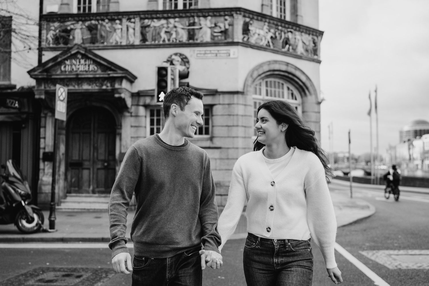A couple strolls along a scenic city street with historic architecture in black and white. Surprise proposal dublin photography