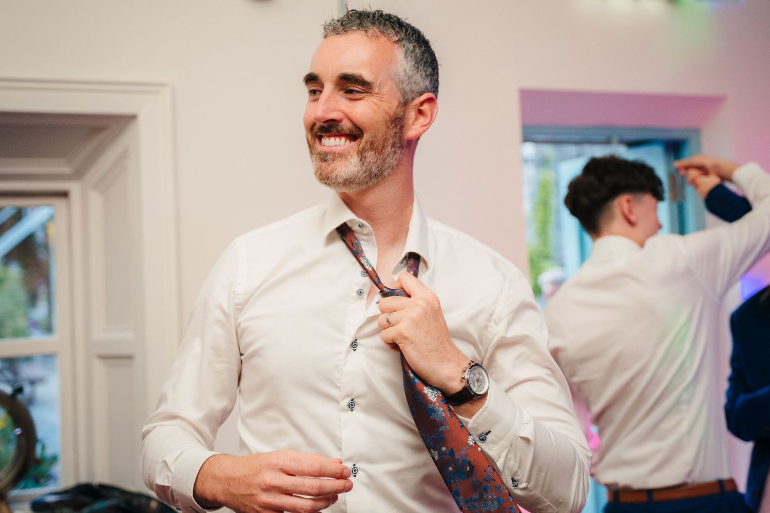 A person in a white dress shirt adjusting their tie while smiling. . Village Barn Tyrrellspass wedding photographer Ireland