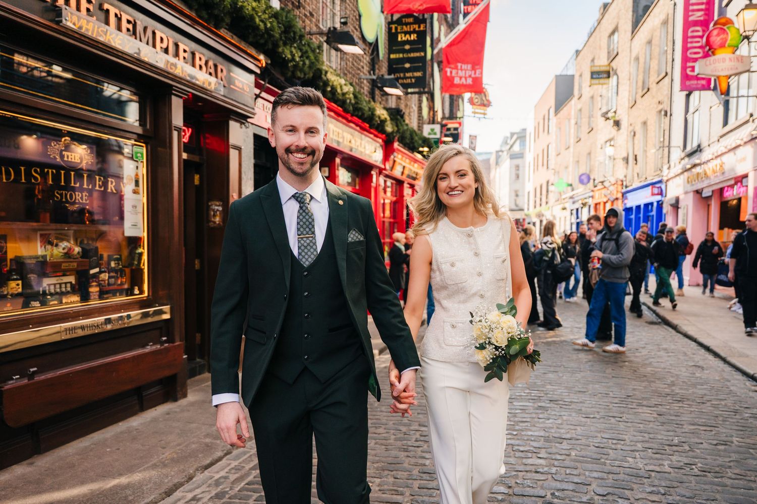 A happy couple walks along a cobblestone street lined with shops and festive decorations. City Hall Dublin wedding photogrAPher