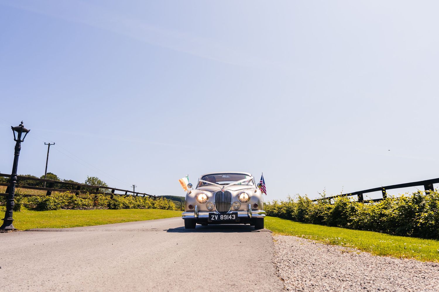 Poulaphouca Wedding photographer wicklow  Classic white vintage wedding car driving down sunny country road.