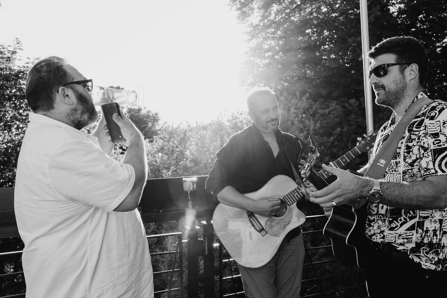 Poulaphouca Wedding photographeMusicians perform at an outdoor event with one singing and others playing acoustic guitar in black and white.
