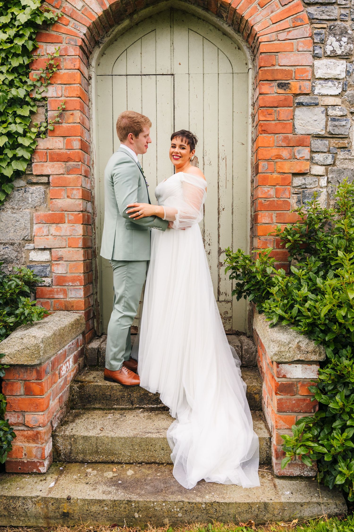 Millhouse slane wedding photographer dublin Newlyweds share a tender moment in front of an arched brick doorway with climbing ivy.