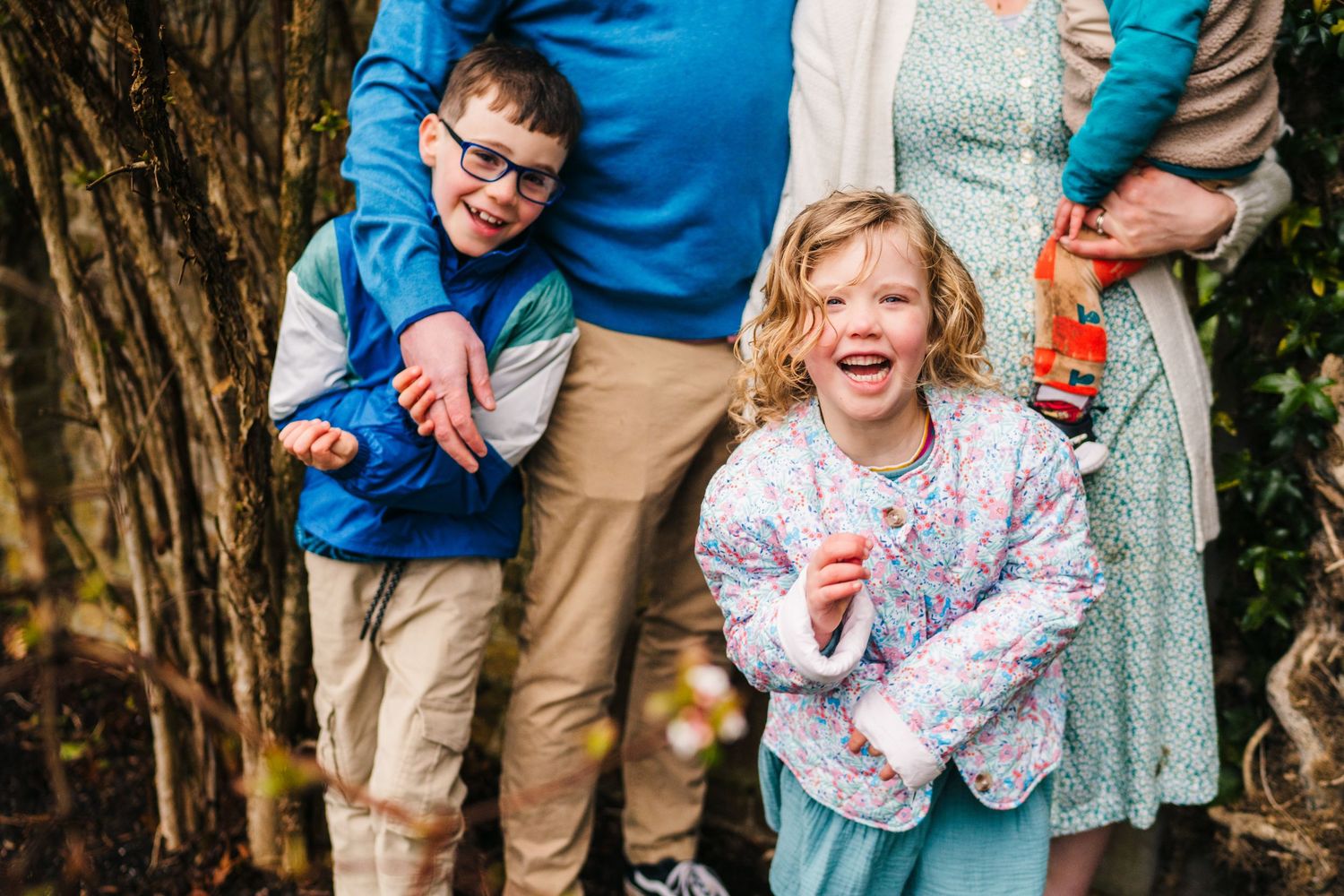 Group of people laughing together outdoors near bushes during a casual photo session. Family photographer Dublin Ireland