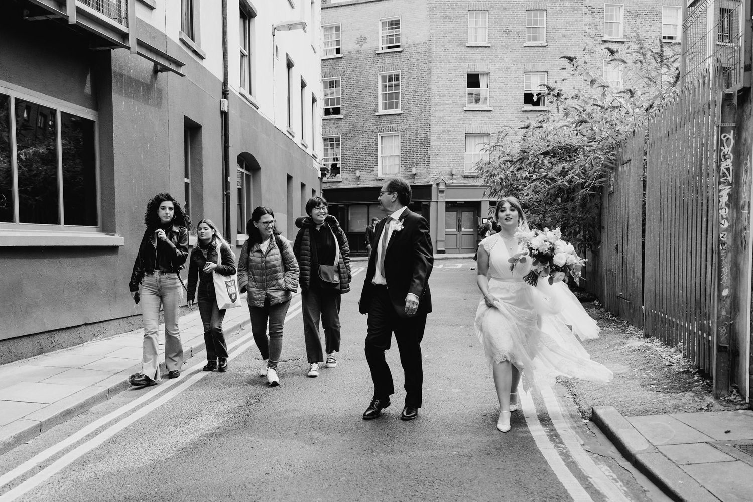 Wedding party walking down a city street in black and white photography. PHOTOGRAPHER Dublin Ireland Wedding