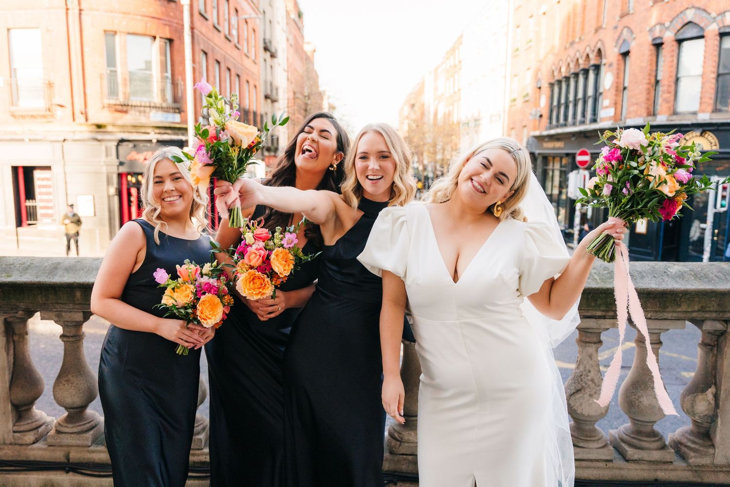 Wedding party in black dresses and white gowns pose together in an elegant venue with floral bouquets. Wedding photographer dublin