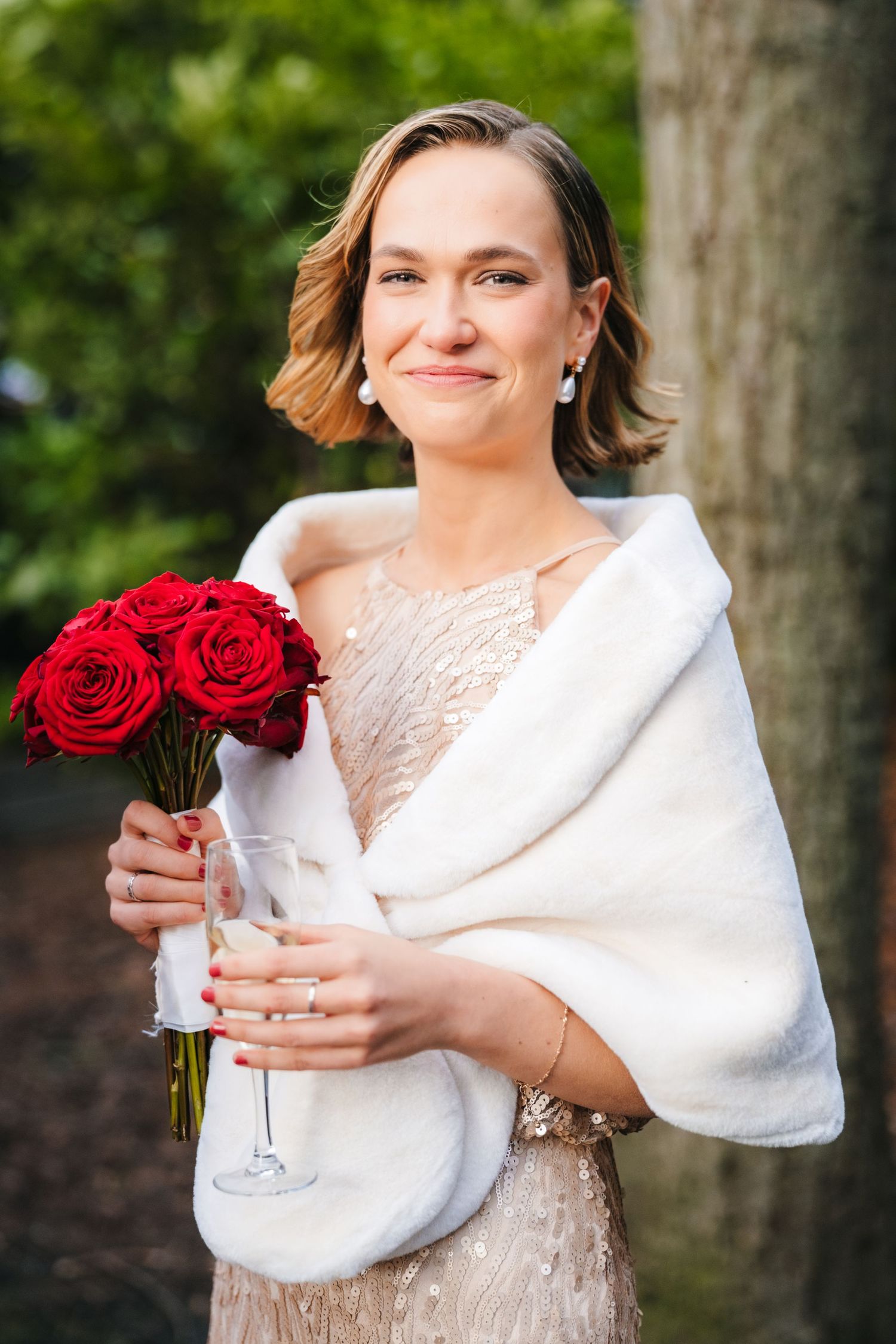 A bride in a white lace dress and fur wrap holds red roses against a natural outdoor background.Stephens green club dublin Wedding photograp
