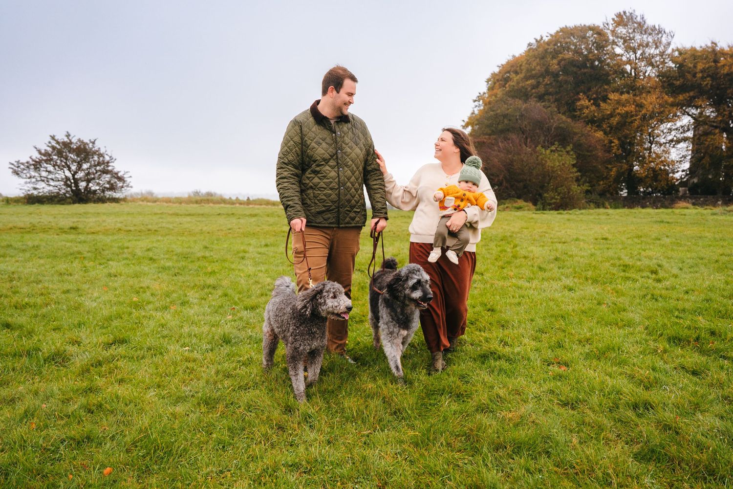 A person and two husky dogs play together in a green grassy field on an autumn day. Family photographer Dublin