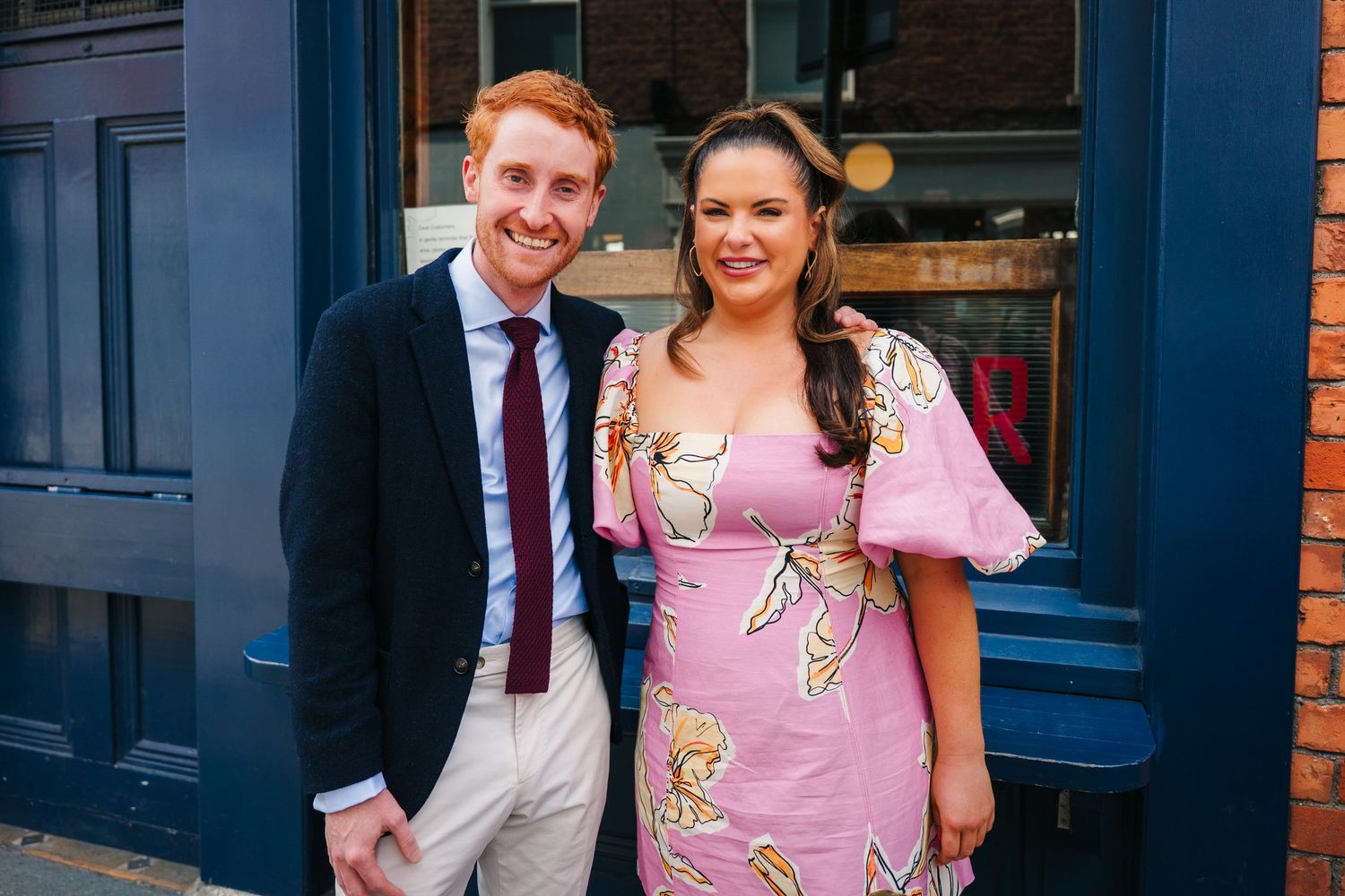 Festive gathering outside blue-trimmed brick building on sunny day. Same sex wedding PHOTOGRAPHER Dublin
