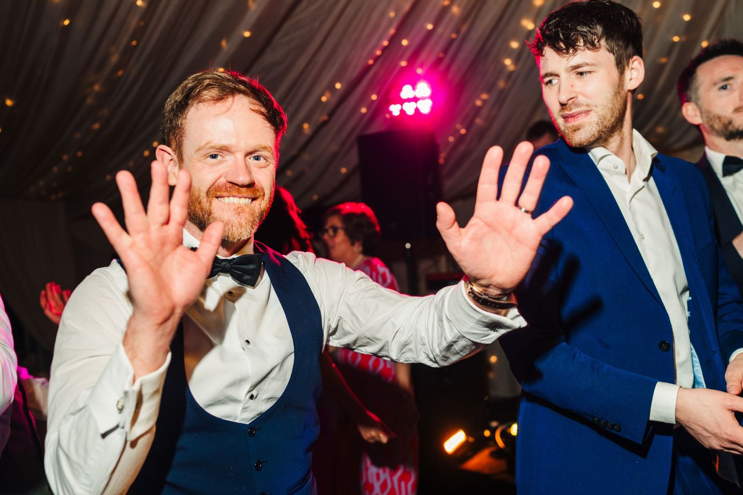Castle Leslie Wedding Photographer Dublin Wedding guests wave and dance under colorful party lights at a reception.