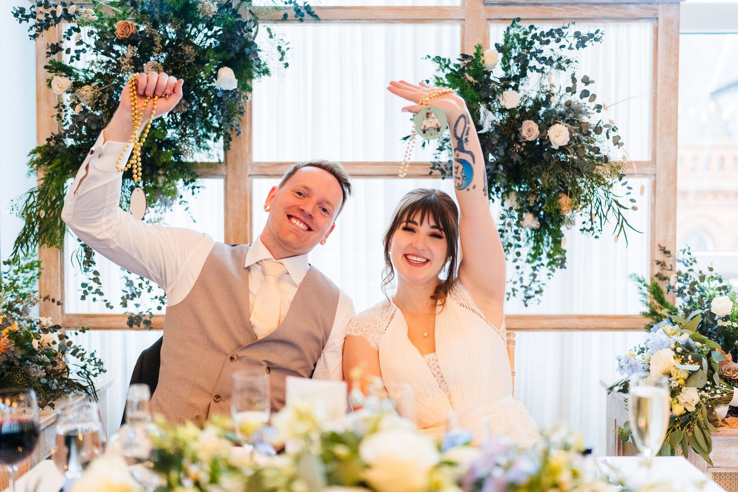 Wedding guests raise arms in celebration under floral arch during indoor reception. PHOTOGRAPHER Dublin Ireland Wedding