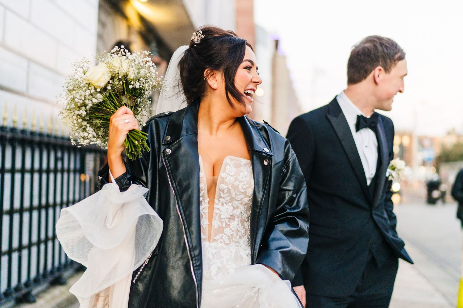 A couple walking outdoors with the bride wearing a leather jacket over her wedding dress. Wedding PHOTOGRAPHER Dublin