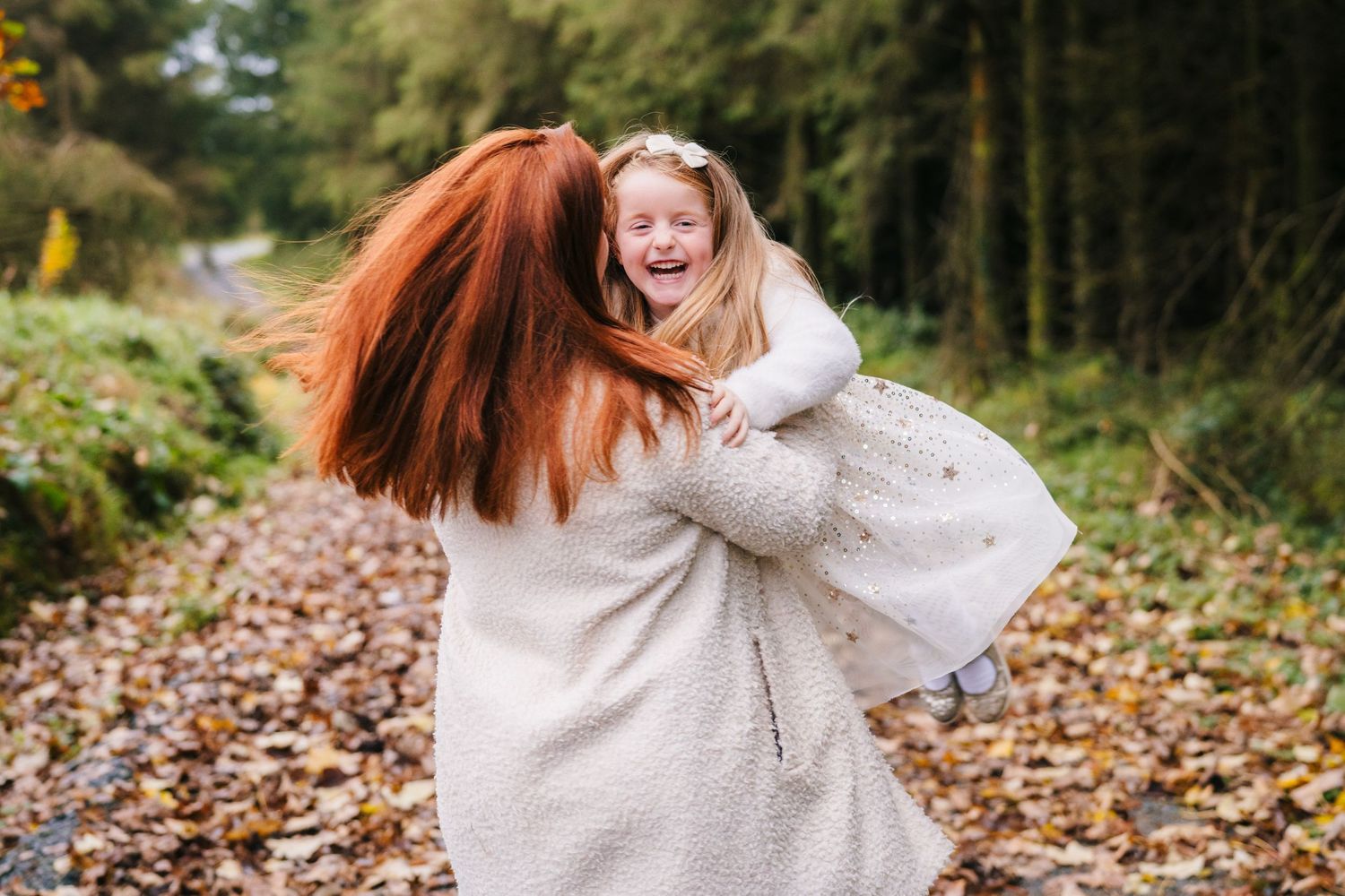 A joyful embrace between two people on an autumn day surrounded by fallen leaves in a wooded setting. Family Photographer Dublin Ireland
