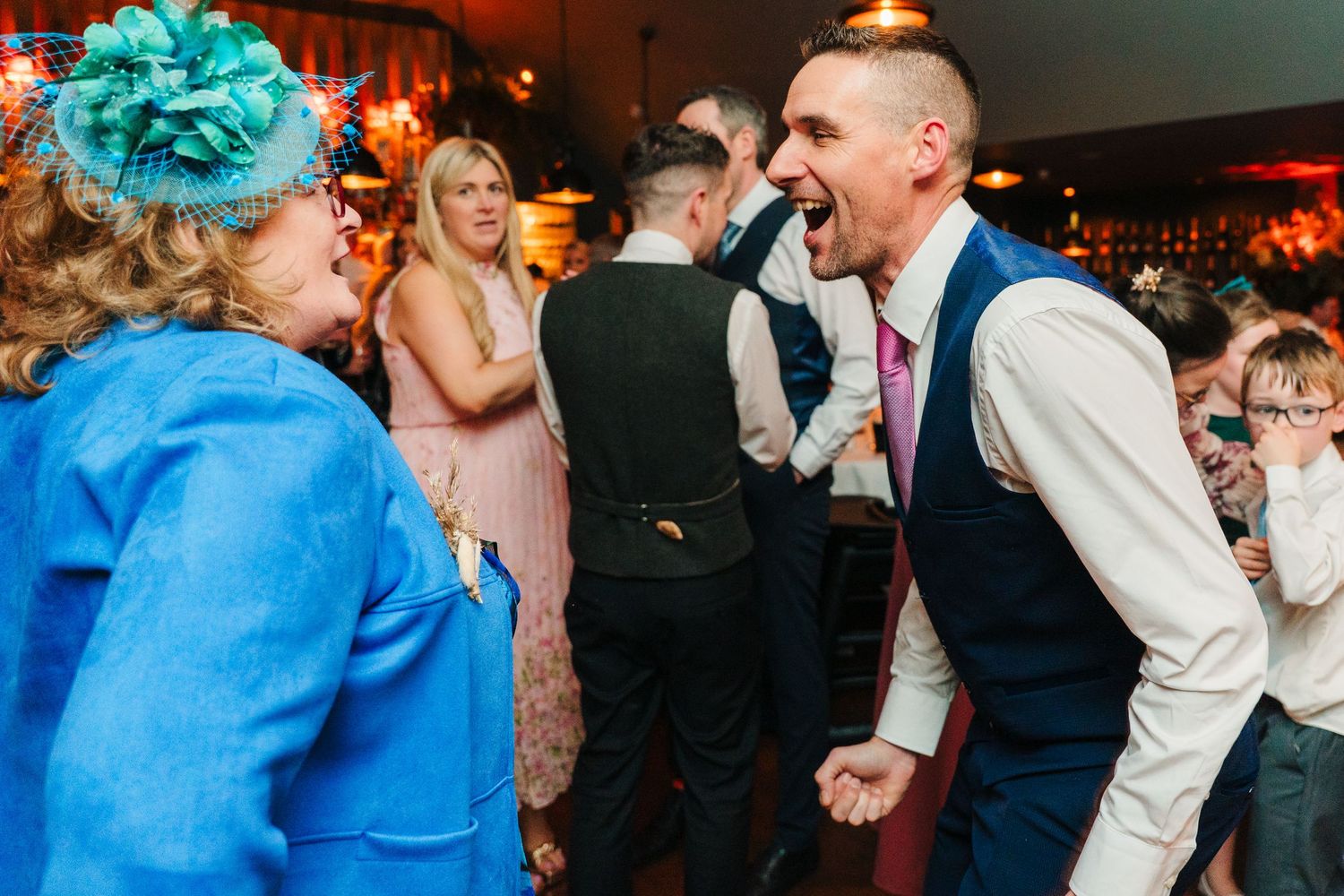 Guests enjoying a lively dance party at a dimly lit indoor reception venue with blue decor accents. Marco Pierre Dublin Wedding Photographer