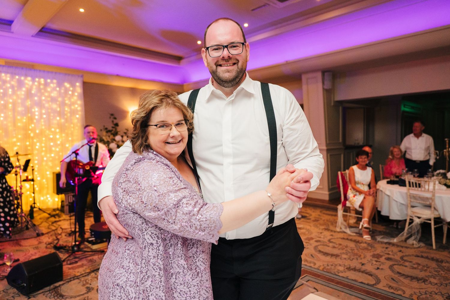 A couple dances together at a wedding reception with twinkle lights and purple lighting in the background. Portmarnock Hotel Wedding PHOTOGR