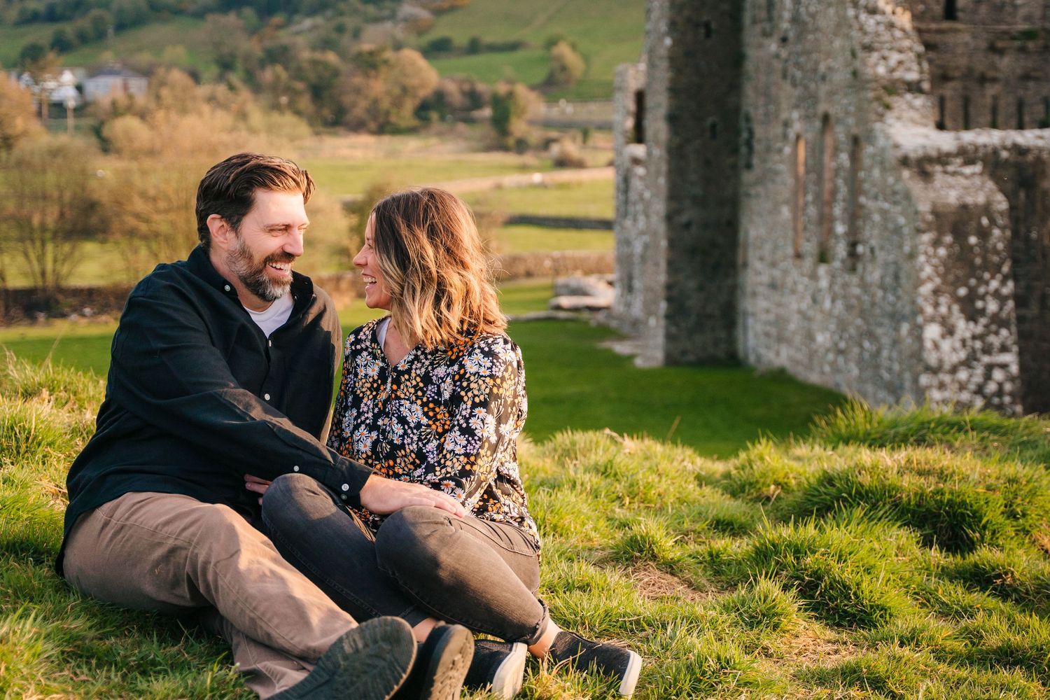 Candid moments of couple enjoying themselves on grassy hill by ancient castle ruins. Photographer Ireland dublin