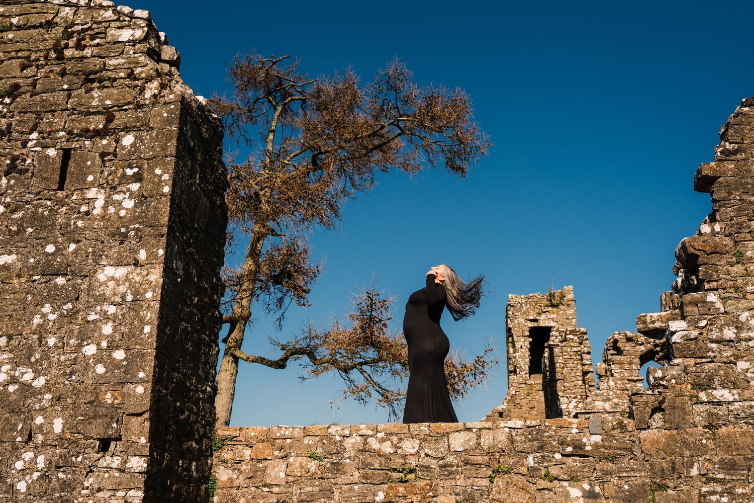 Dramatic silhouette against bright blue sky between ancient stone walls with bare tree. Family PHOTOGRAPHER Dublin