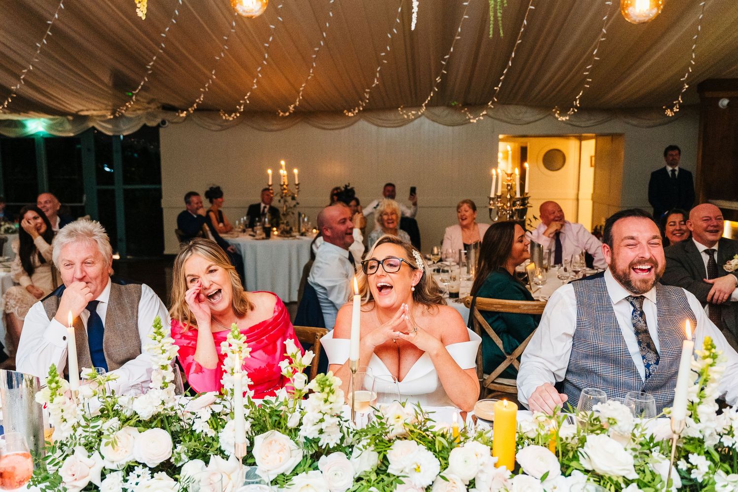 Long banquet table adorned with white floral centerpieces and glowing candlelight during evening wedding reception.  Virginia Park Lodge Wed