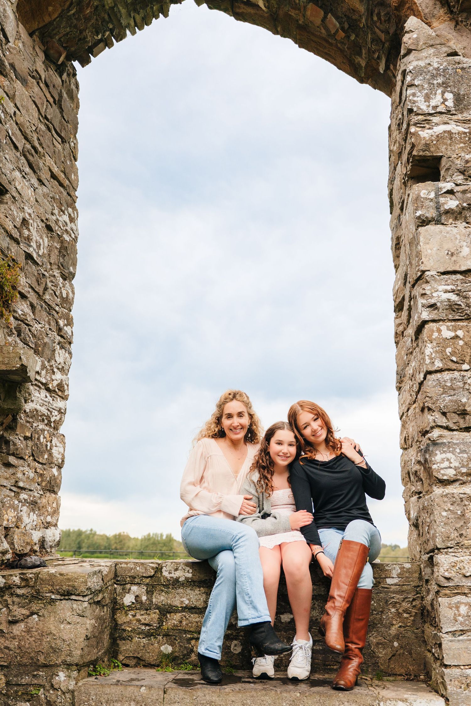 Friends relaxing under ancient stone arches at a historic site on a cloudy day. BEctive abbey family photographer dublin