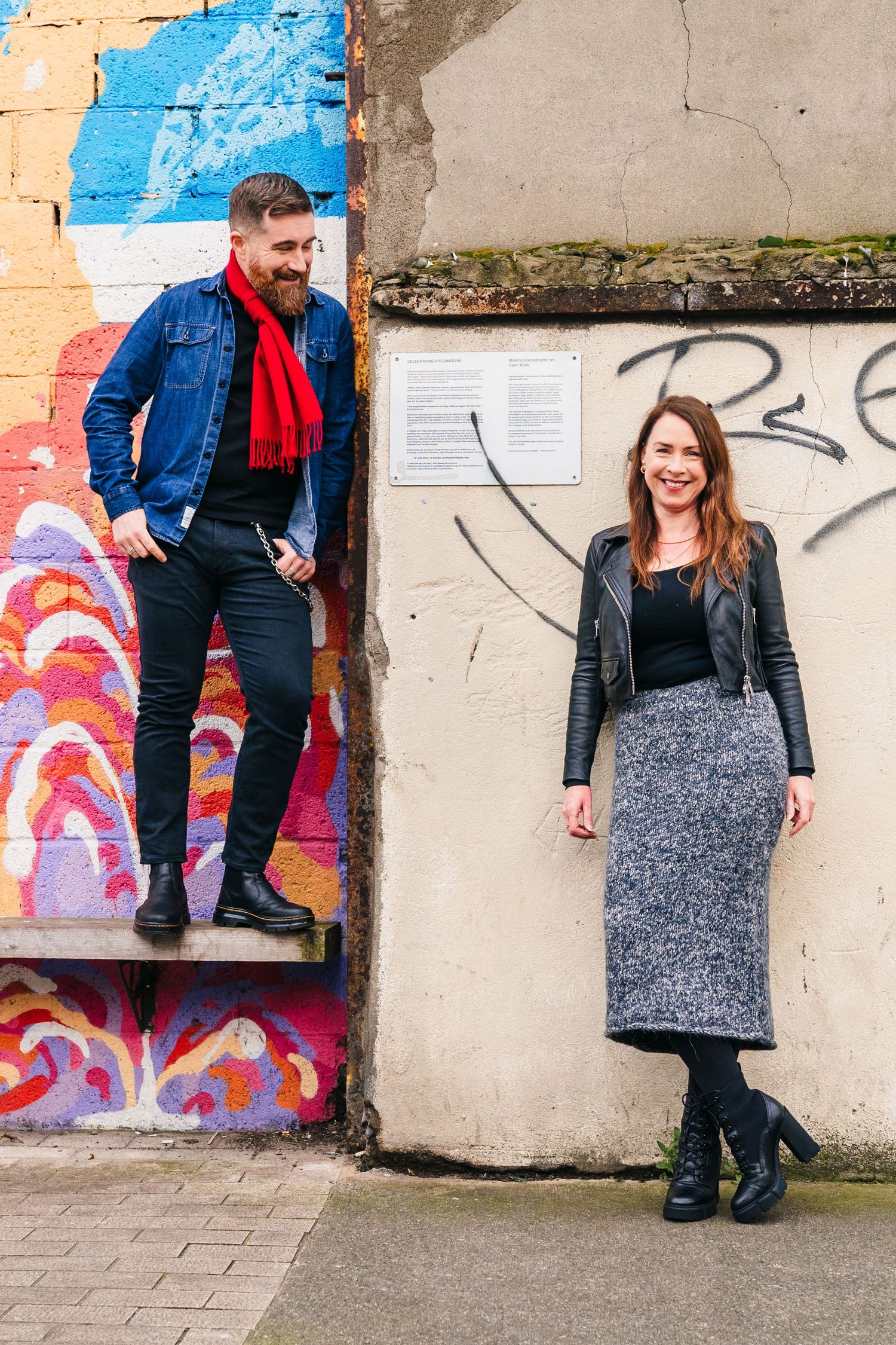 A couple poses against a graffiti-covered wall in matching casual outfits with boots. PHOTOGRAPHER Dublin