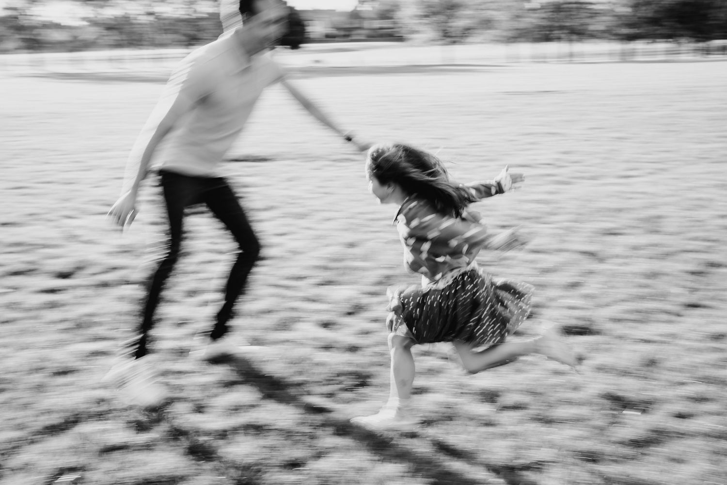 A black and white motion-blurred photograph of two people dancing and twirling together on a beach. family PHOTOGRAPHER Dublin