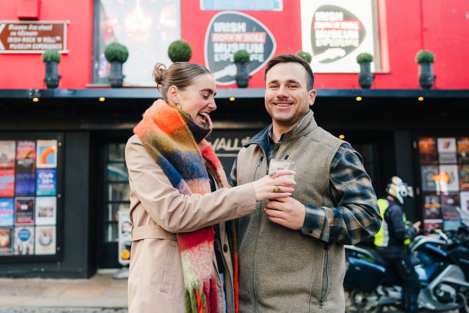 Two people sharing a warm moment and laughing together against a bright red storefront background. PHOTOGRAPHER Dublin
