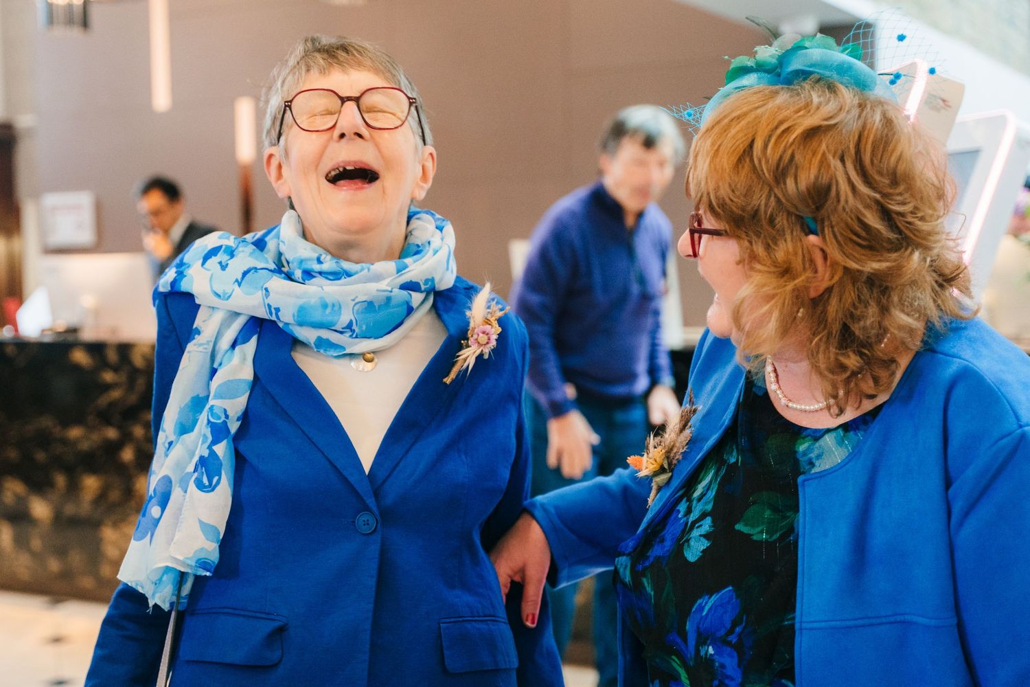 Two guests wearing matching bright blue jackets share a joyful moment at a celebration. Marco Pierre Dublin Wedding Photographer