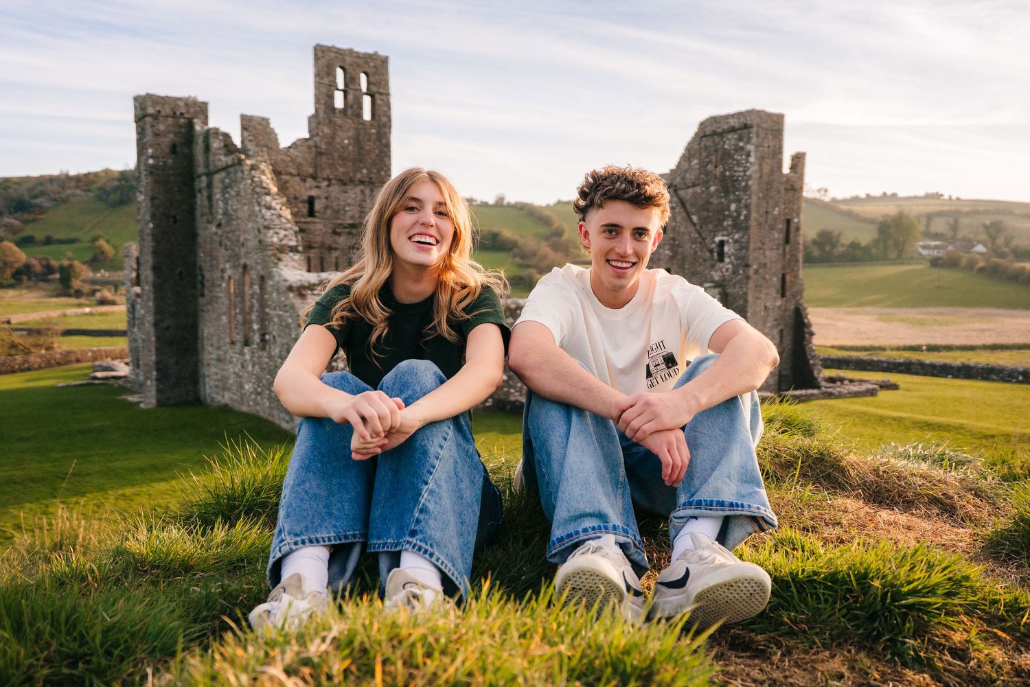 Natural candid moments captured between couple sitting on grassy hill by castle ruins. Photographer Ireland dublin