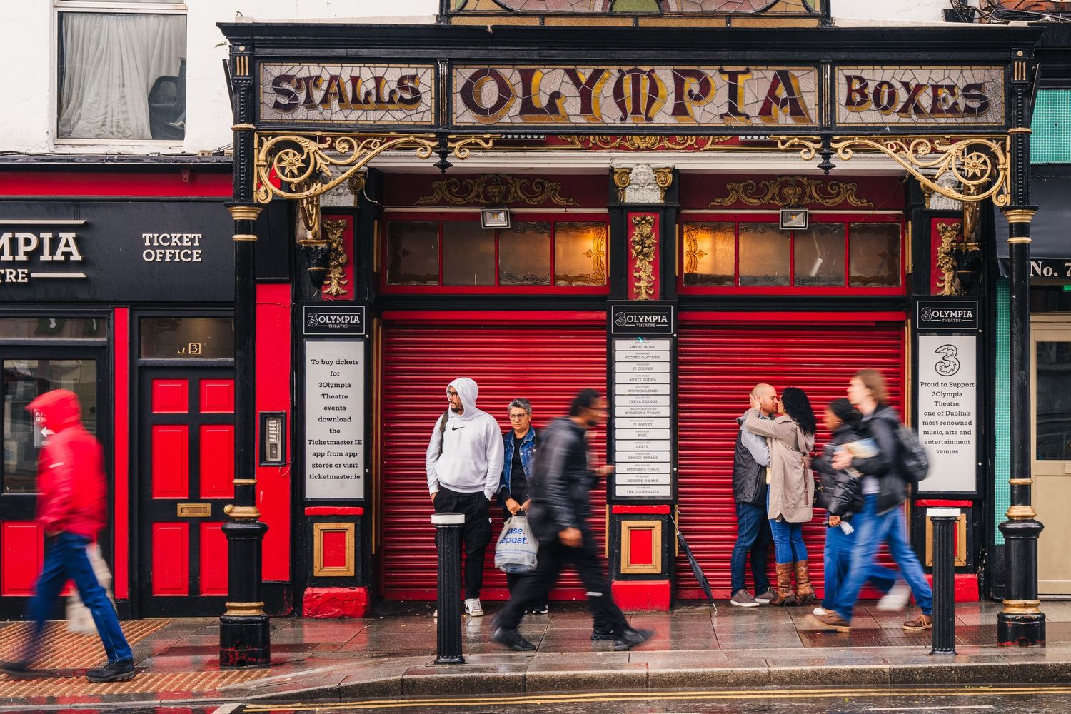 Storefront of Olympia boxing venue with red shutters and pedestrians walking on London street. Proposal Dublin Photographer