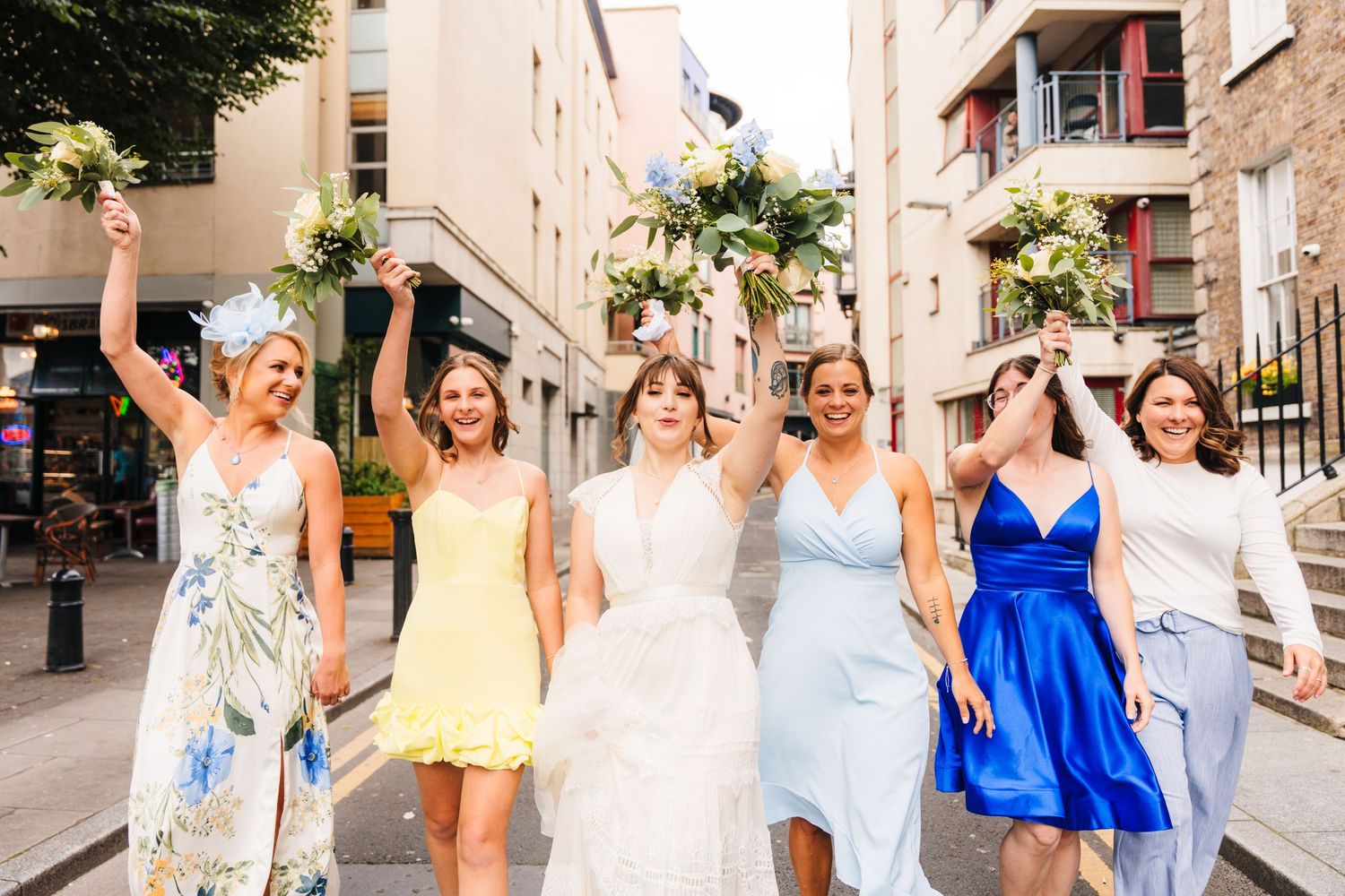Bride and bridesmaids celebrating joyfully while walking down city street. PHOTOGRAPHER Dublin Ireland Wedding