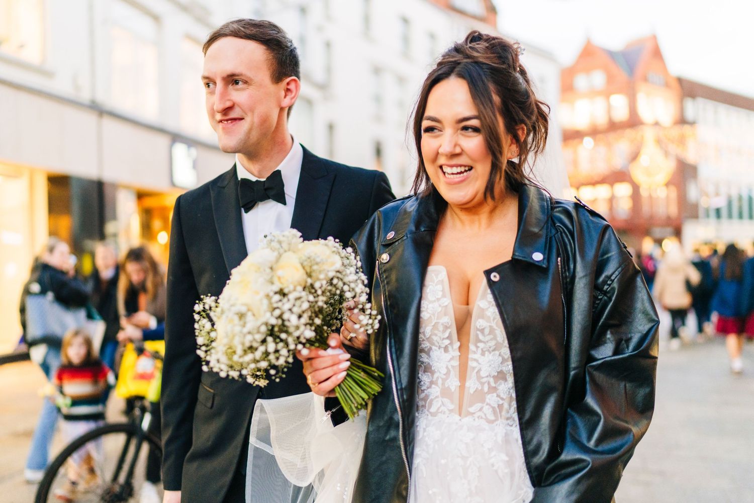 A couple strolls along a city street during their wedding, with the bride wearing a leather jacket. Wedding PHOTOGRAPHER Dublin
