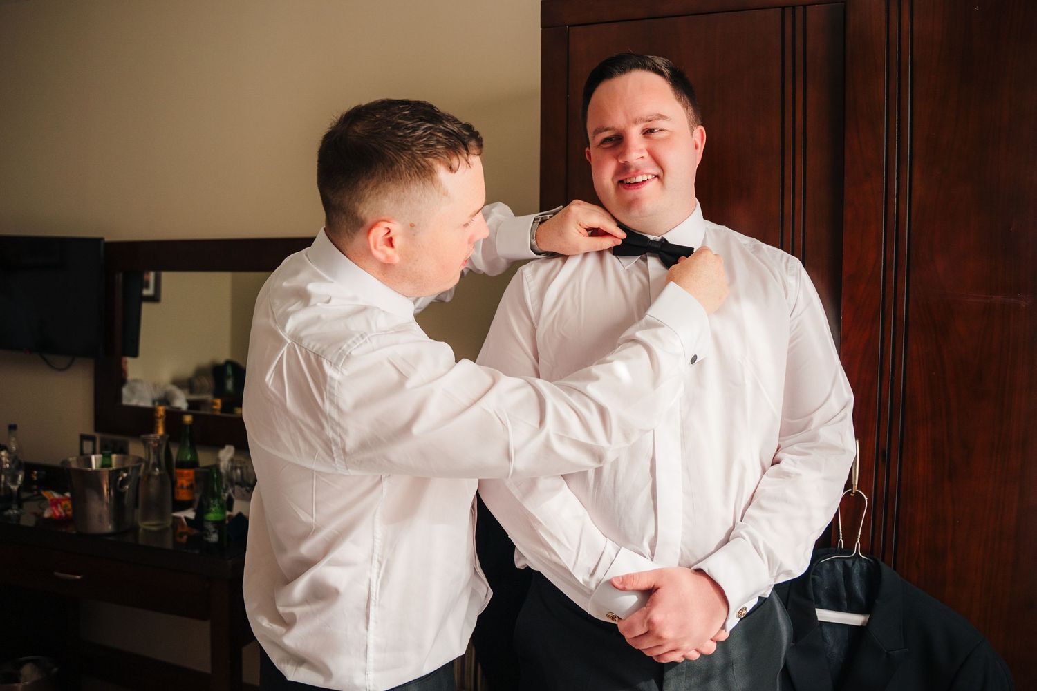 Two people in white dress shirts help each other prepare for a formal event. Wedding Photography Trim Castle Ireland