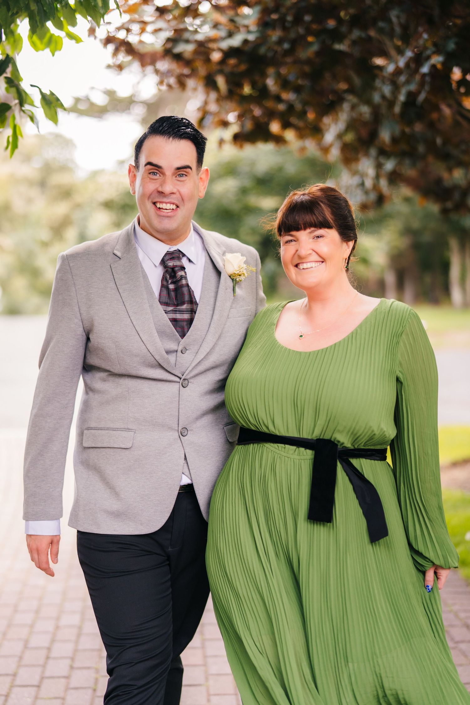 A couple poses outdoors, with the person in a gray suit and the other wearing a flowing green dress with black sash. Portmarnock Hotel Weddi