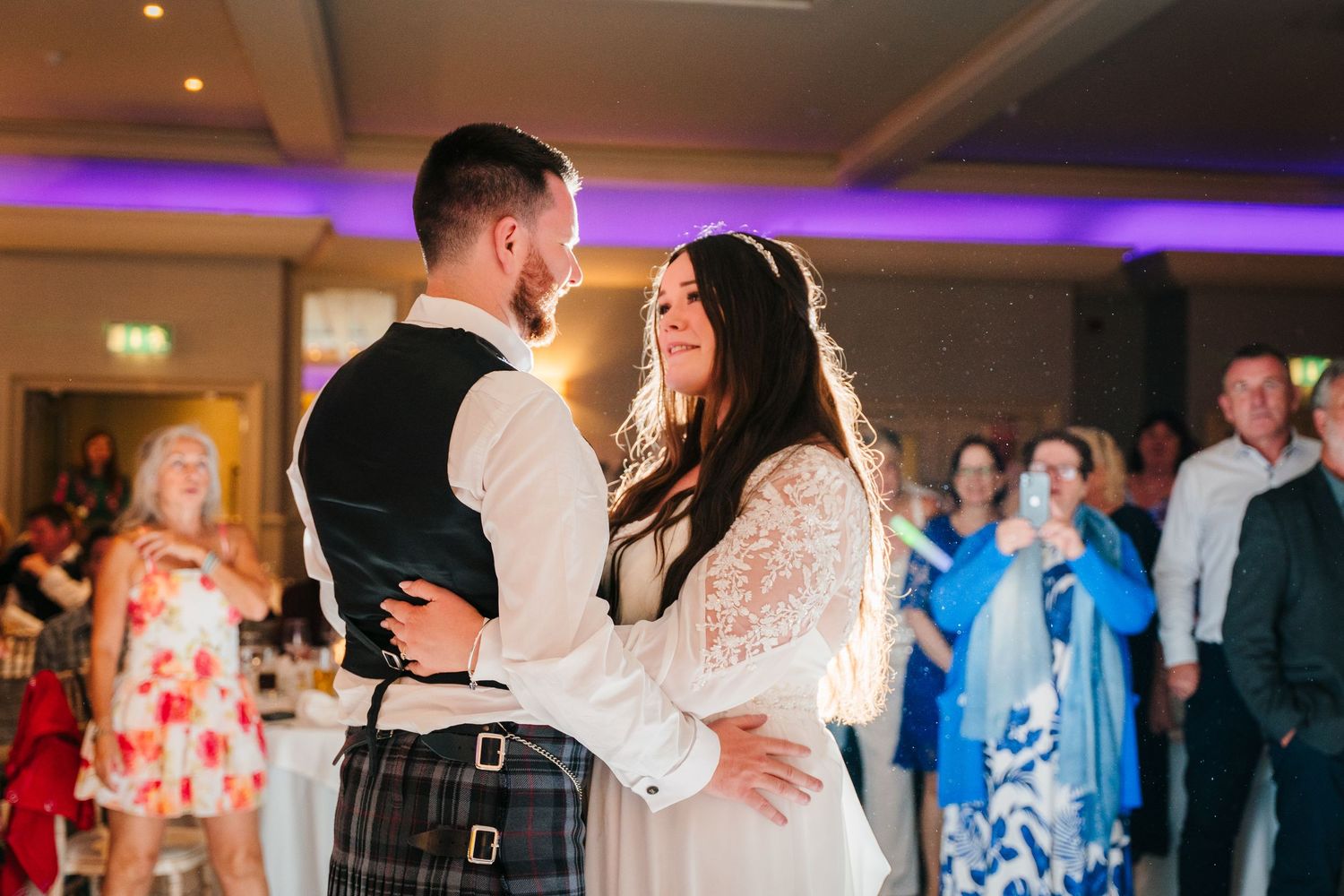 A couple dances their first dance at a wedding reception with guests watching in the background. Portmarnock Hotel Wedding PHOTOGRAPHER Dubl