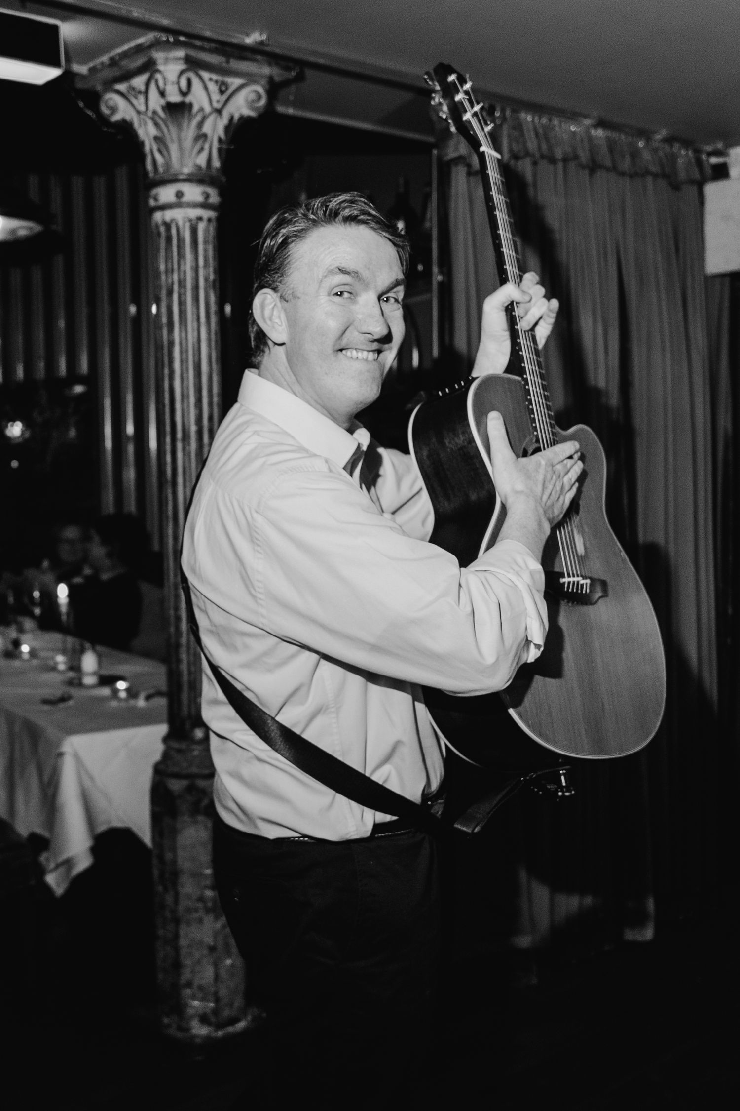 A musician poses with an acoustic guitar in a vintage black and white photo inside a venue. Marco Pierre Dublin Wedding Photographer