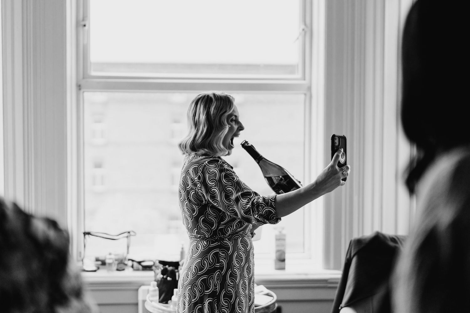 A person in a floral dress takes a selfie in front of a bright window during a party gathering. House Dublin Wedding Photographer