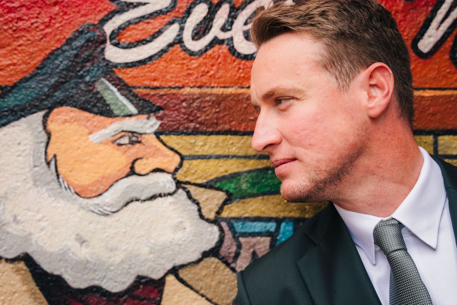 A suited person poses next to a colorful street art mural featuring a cartoon character. Wedding photographer dublin