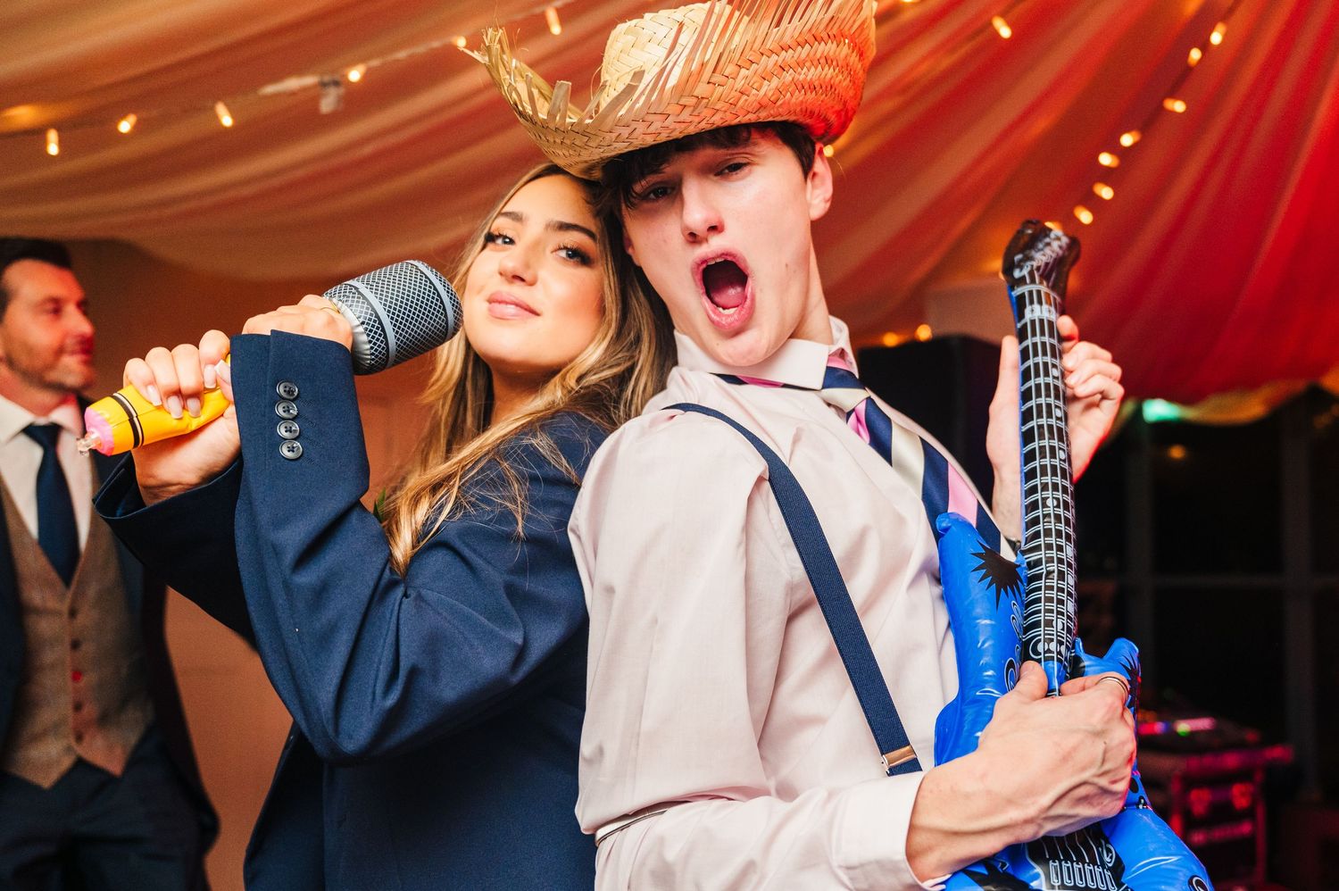 People singing and dancing at a lively wedding reception under red drapery with string lights. Wedding Photographer Dublin Ireland