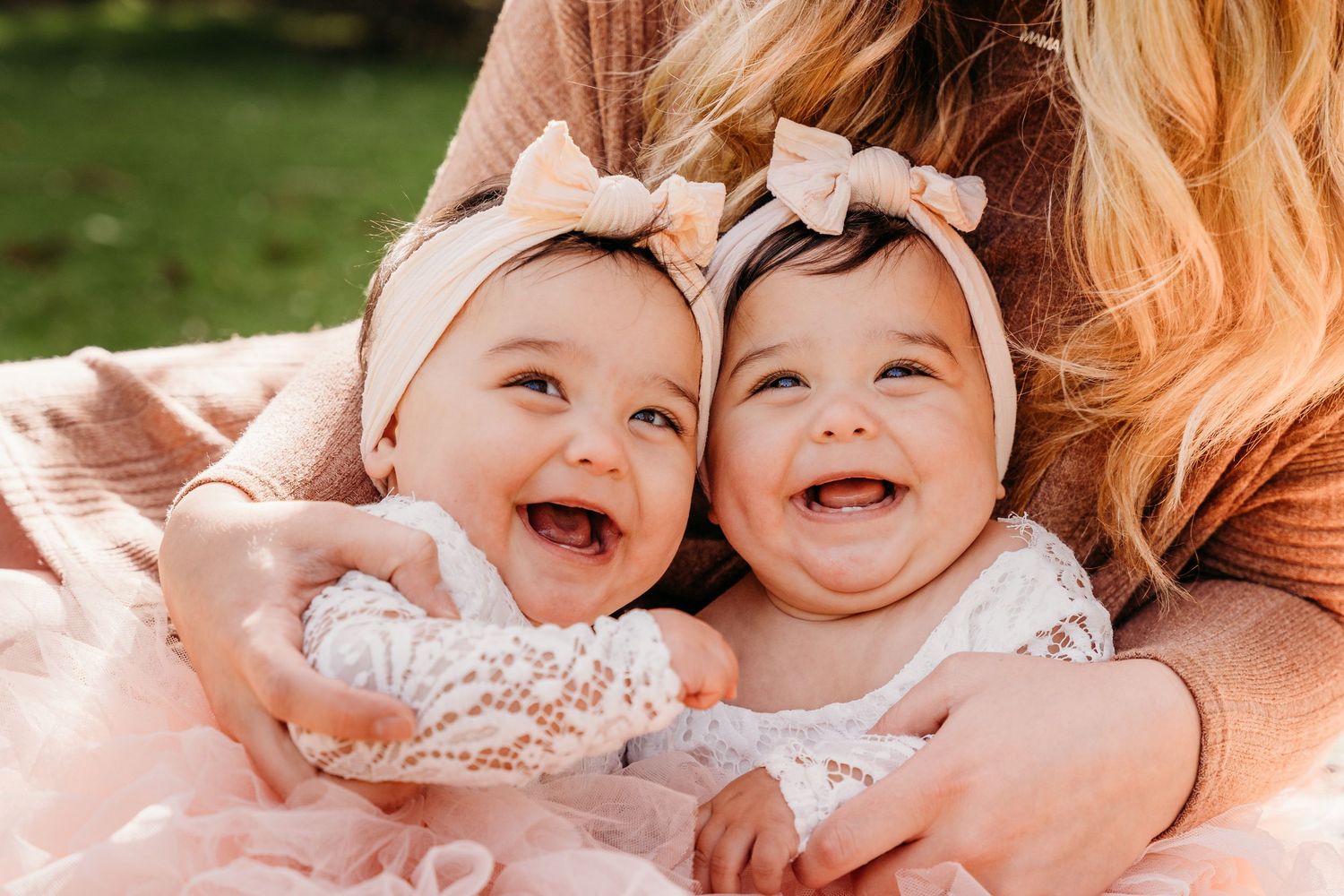 Row of joyful babies in white and pink outfits lying together on a blanket outdoors. family PHOTOGRAPHER Dublin