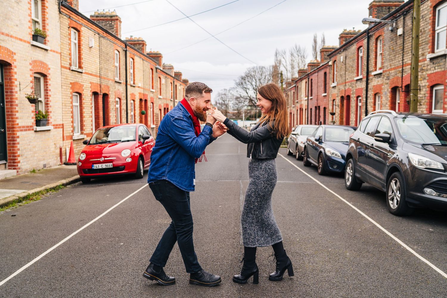 A couple dances playfully in the middle of a residential street lined with brick houses and parked cars. PHOTOGRAPHER Dublin
