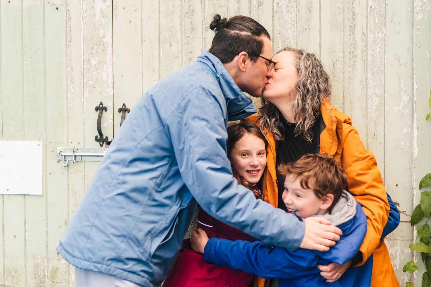 Family sharing a warm embrace and laughing together against a rustic white barn door. family PHOTOGRAPHER Dublin