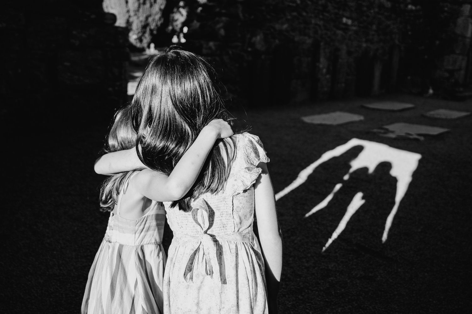 Two children in white dresses look at creepy shadows cast on the ground in black and white photography. family PHOTOGRAPHER Dublin