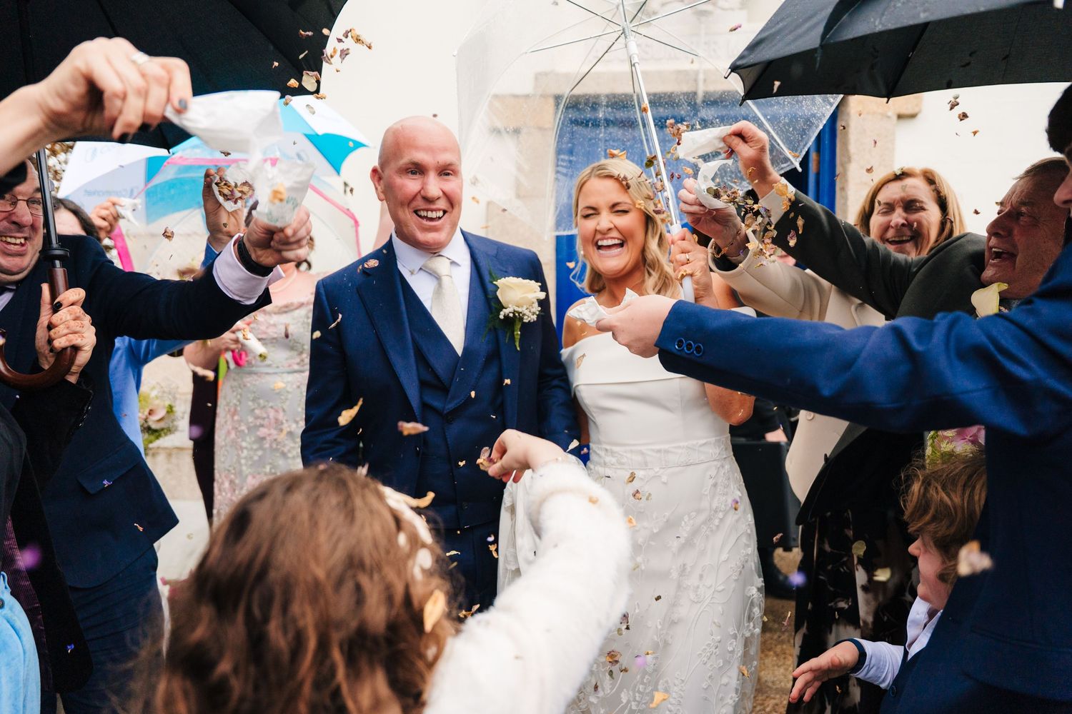 Wedding couple celebrates under confetti shower with umbrellas and guests cheering during outdoor ceremony. The Dean Dublin Wedding Photogra