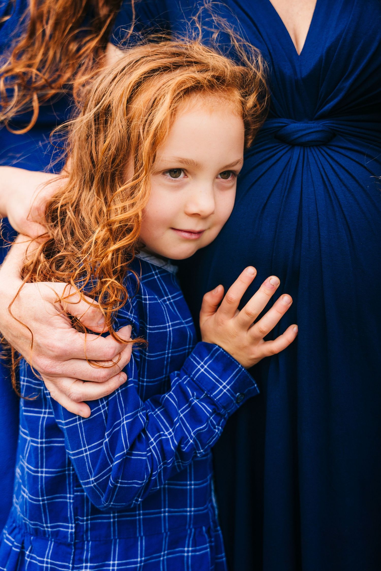 Child in blue plaid shirt hugging a person wearing a navy blue dress.Family photogrAPHER DUBLIN