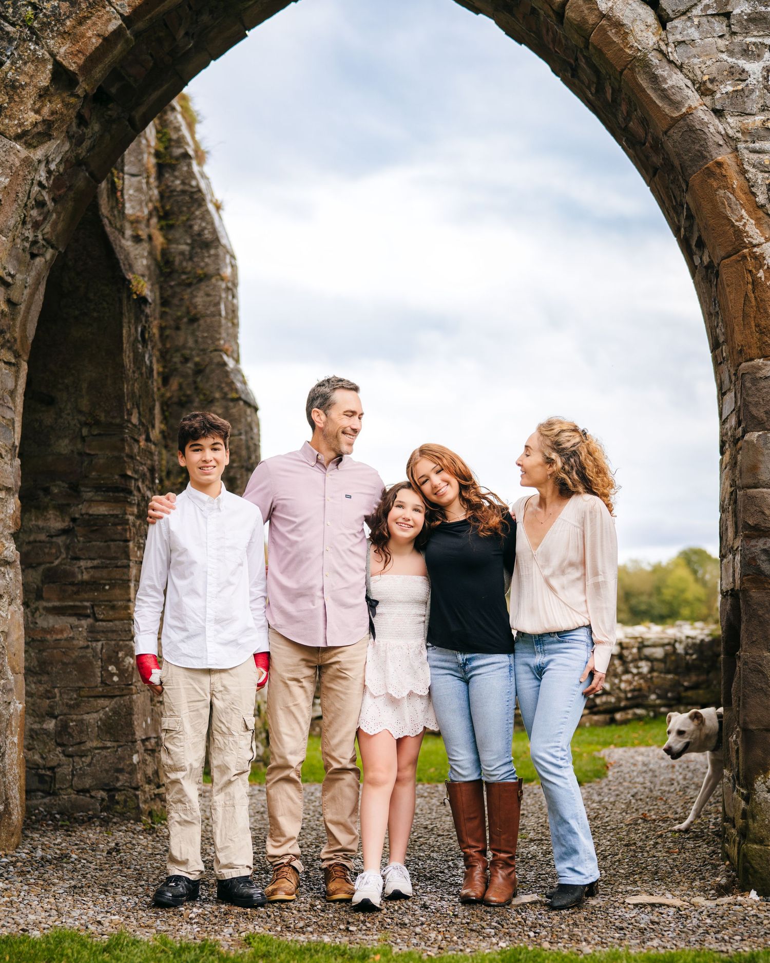 Family group poses together under a stone archway at historic ruins site. BEctive abbey family photographer dublin