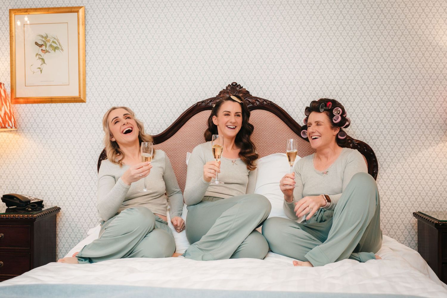 A group in matching sage green sweaters poses playfully together on a white bed.