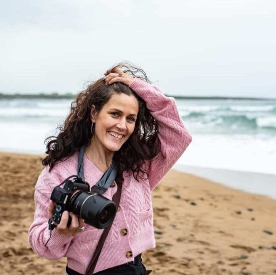 Person with curly hair and a pink jacket taking photos on a windy beach. wedding photographer dublin meath