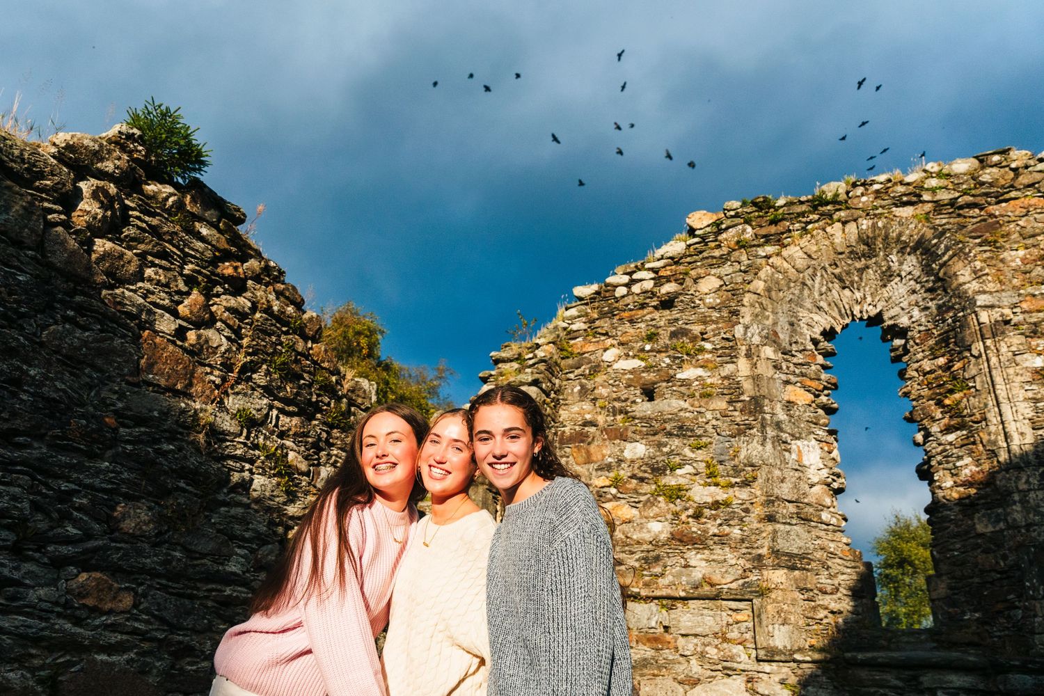 Family photographer Ireland Dublin A group poses in front of an ancient stone wall against a blue sky backdrop.